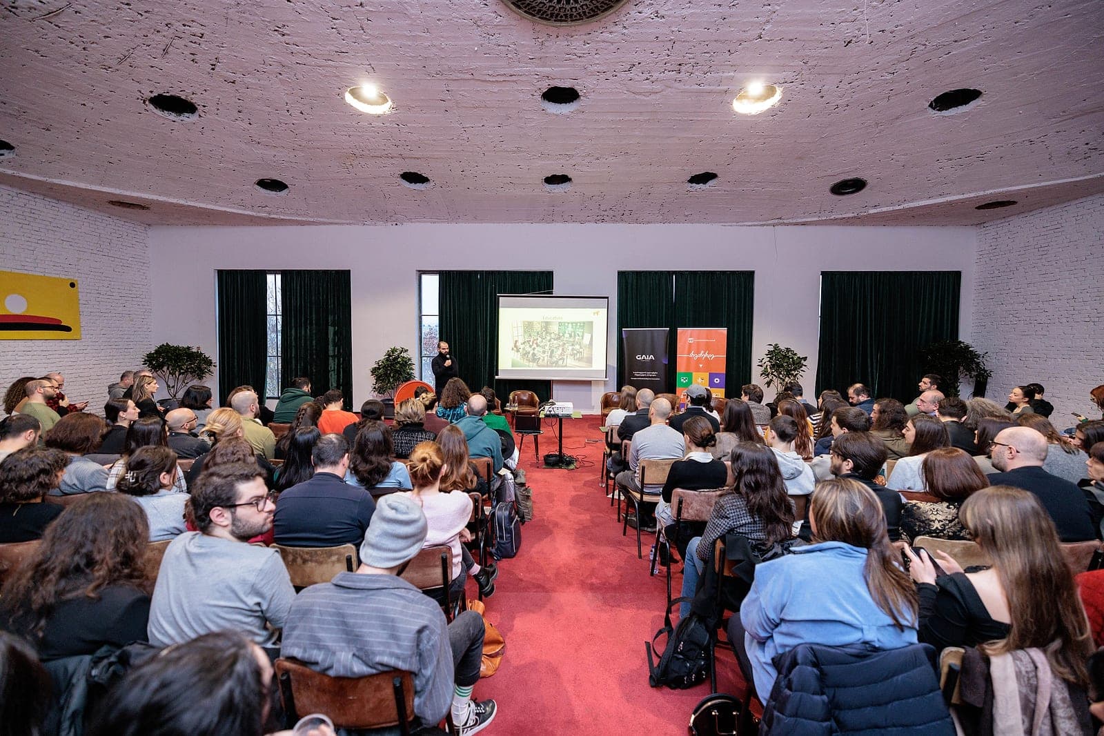 A full room at a GAIA event, with a speaker presenting from the front.